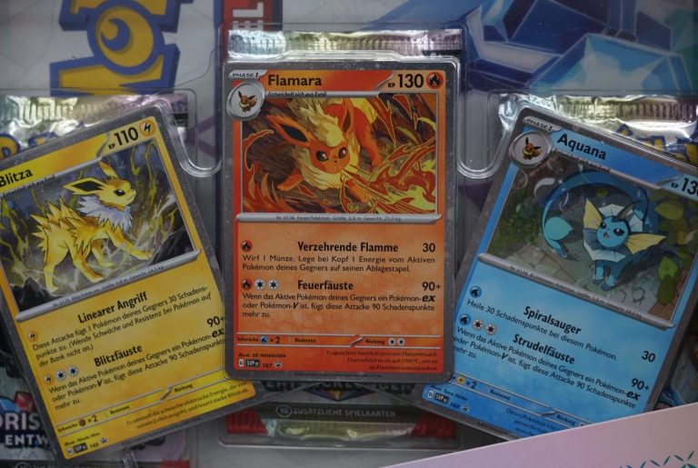 Prismatische ETBs Drei Pokémon-Karten: Flamara, Aquana und Blitza auf einem Hintergrund.